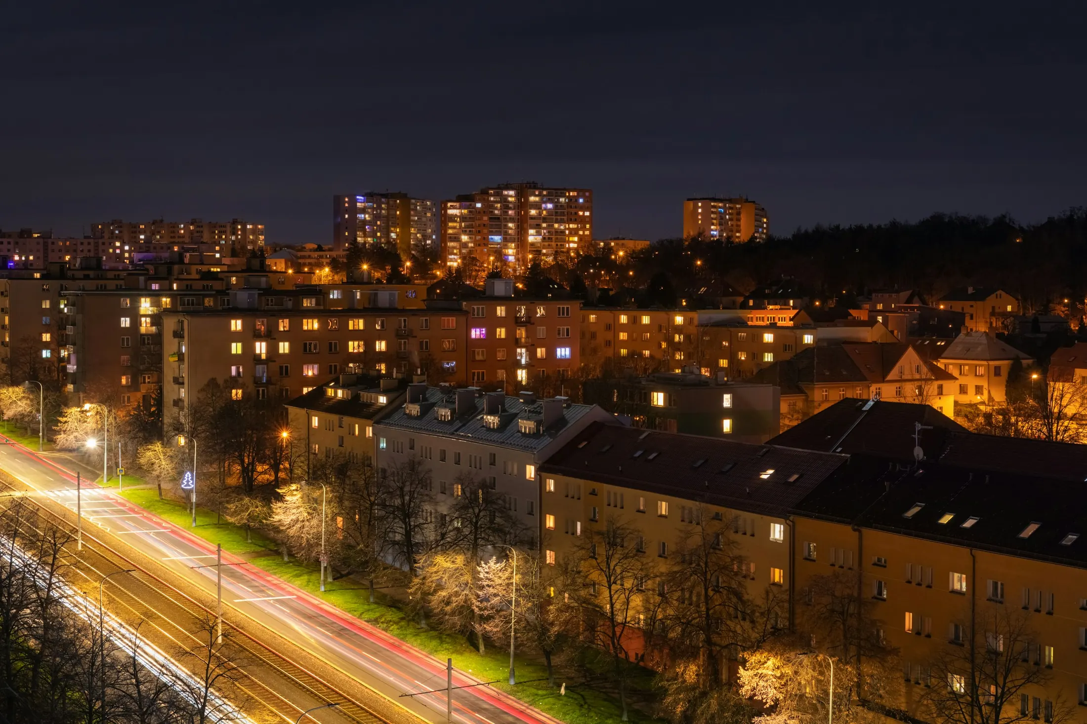 Apartment blocks with lit windows at night above a street with light trails