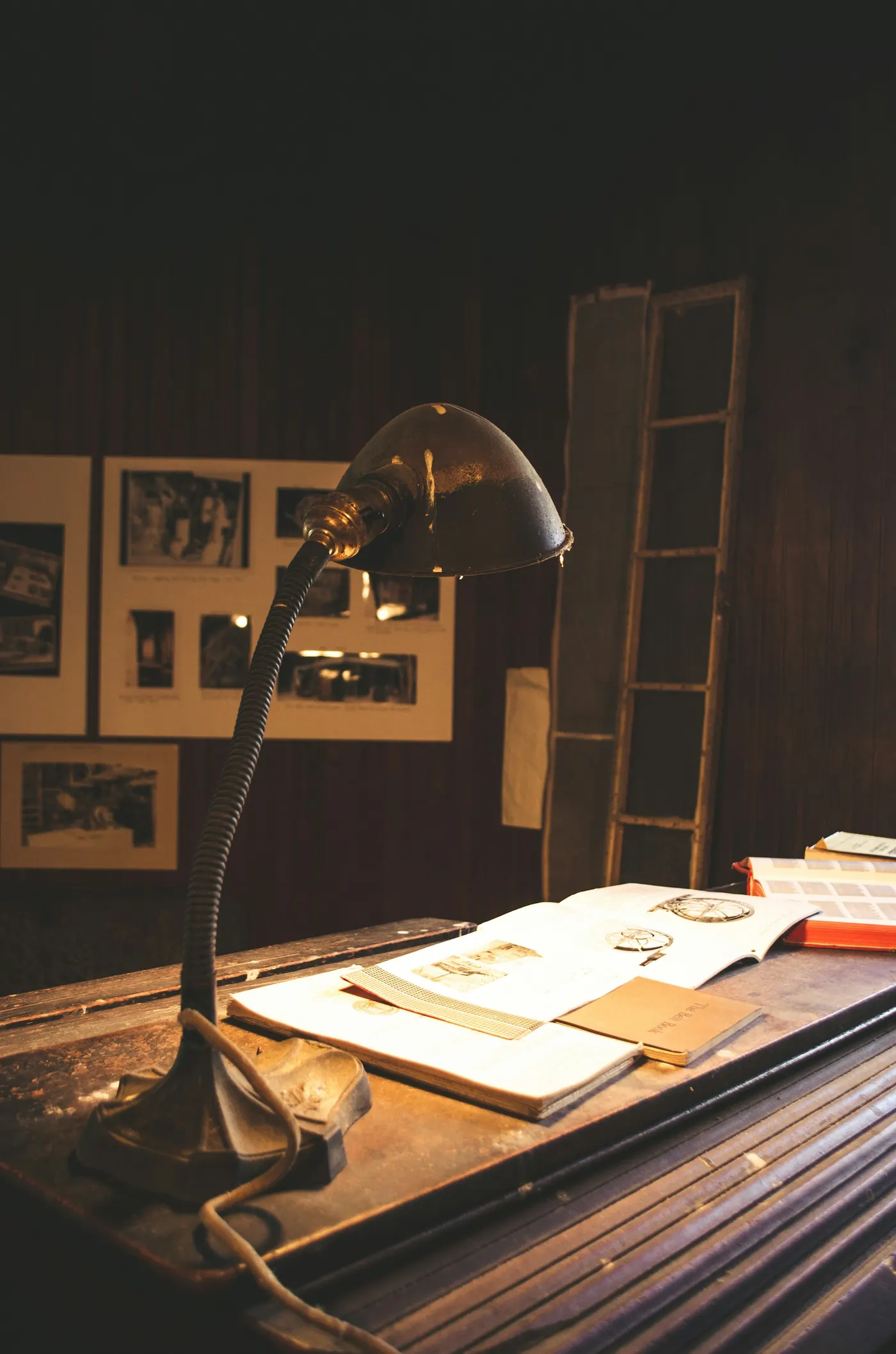A metal desk lamp lighting papers and notebooks on an old wooden desk