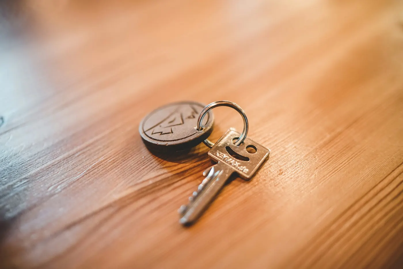 A house key with a round fob lying on a wooden table in warm light